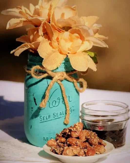 A small plate of Maple Sesame Cacao Beans with Coffee next to a turquoise colored mason jar with orange flowers