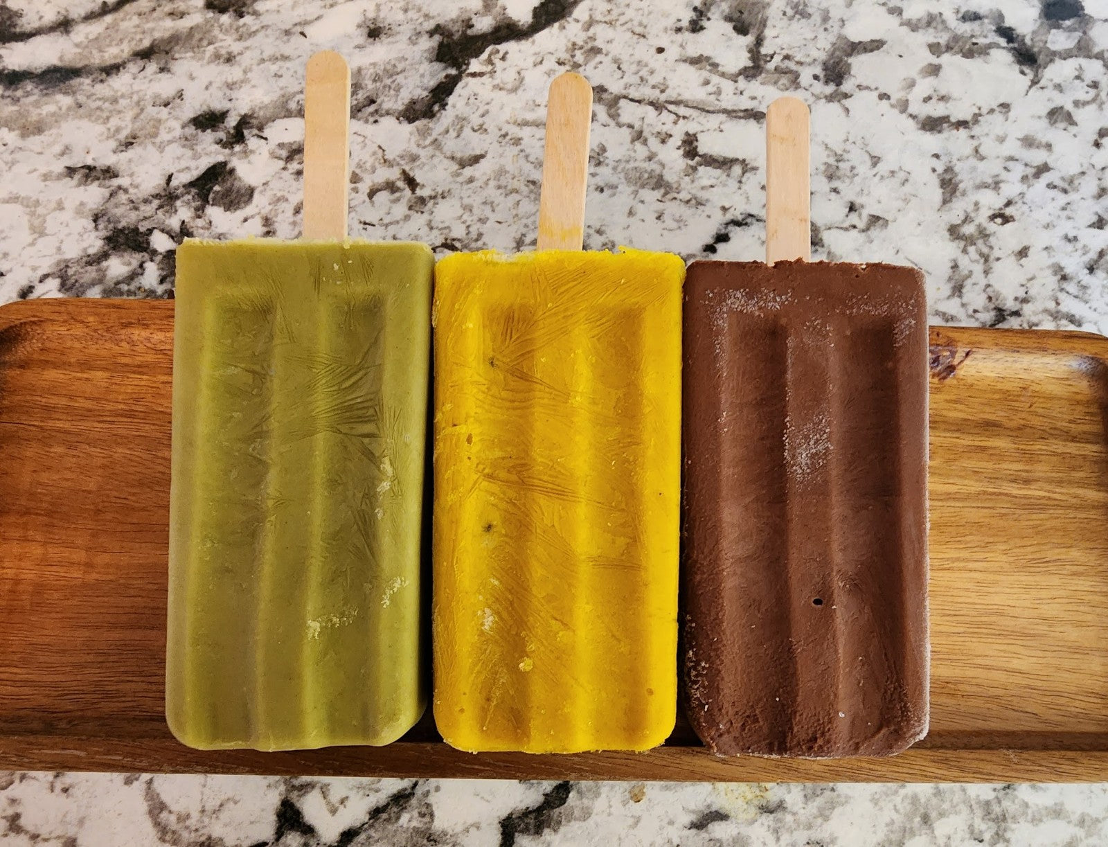 green matcha popsicle on left, golden milk popsicle in the center, and fudge popsicle on the right